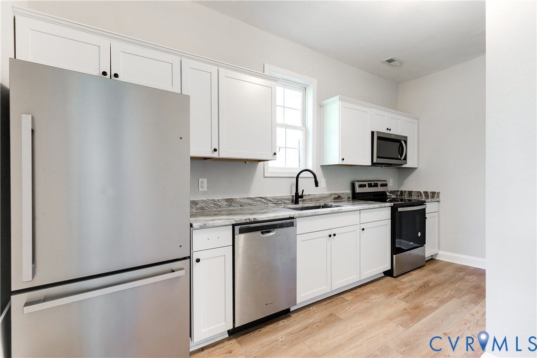 White cabinetry with black hardware, stainless steel appliances, wood-finish flooring, and a window for natural light