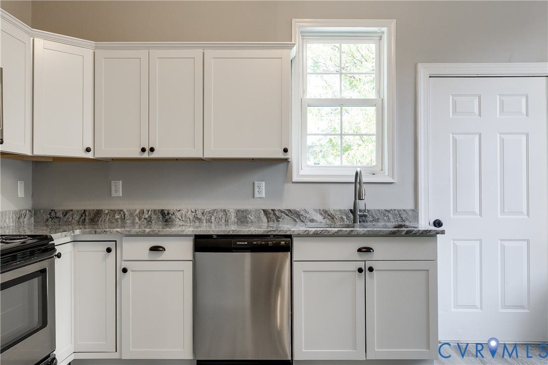 White shaker-style cabinetry with dark hardware, stone countertops with a polished finish, and a stainless steel under-mount sink with a chrome faucet