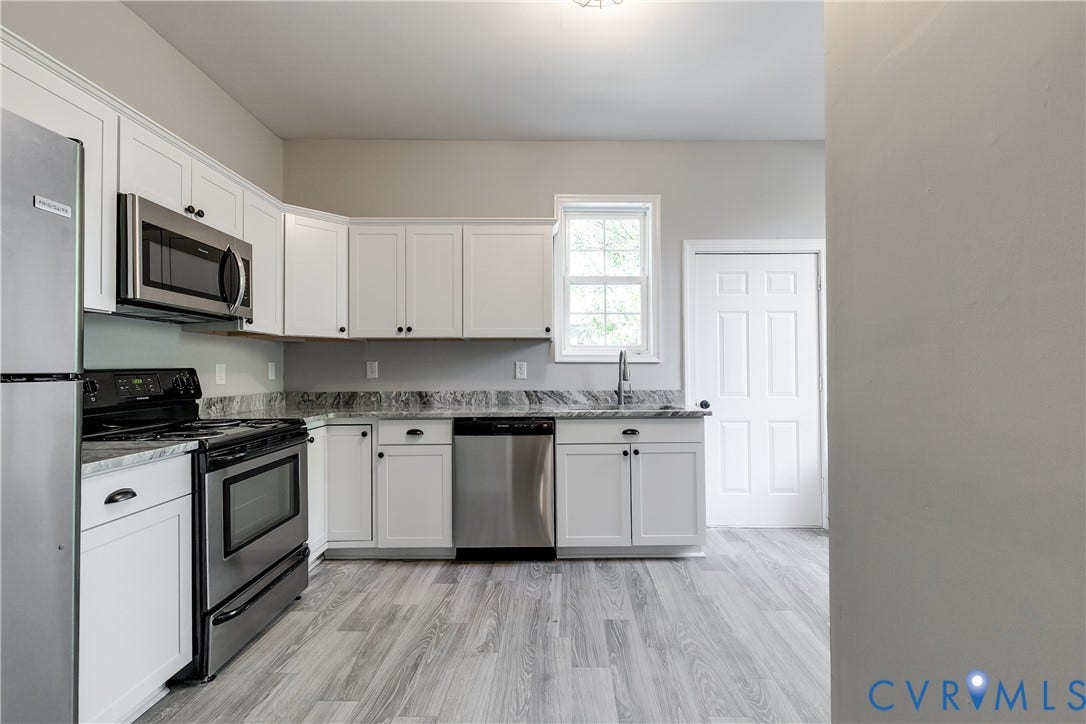 Kitchen featuring white shaker cabinetry, stainless steel appliances, light-toned wood-finish flooring, and a window above the sink