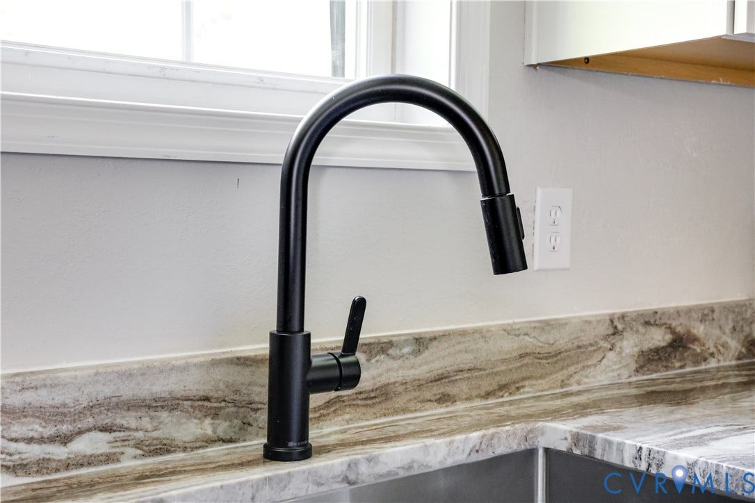 Matte black gooseneck faucet with an integrated sprayer, undermount stainless steel sink, and a variegated stone countertop