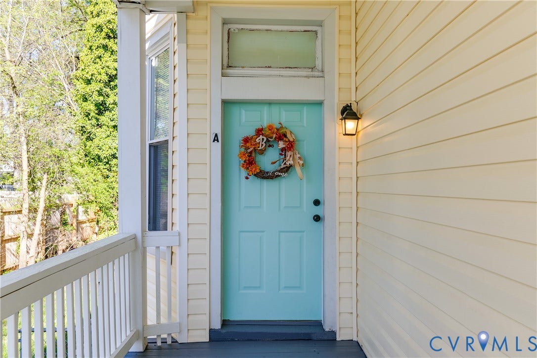 Light blue paneled entry door with transom window, exterior wall lantern, and light yellow horizontal siding
