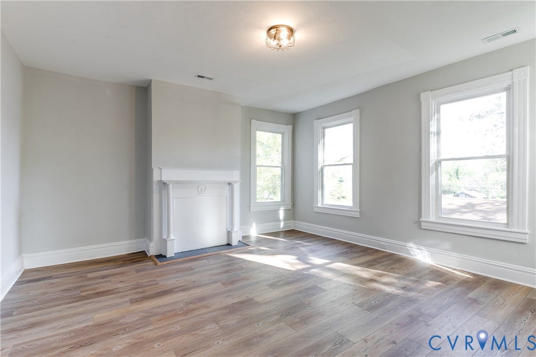 Wood-finish flooring, decorative fireplace, multiple windows with white trim, light-colored walls, and a ceiling-mounted light fixture