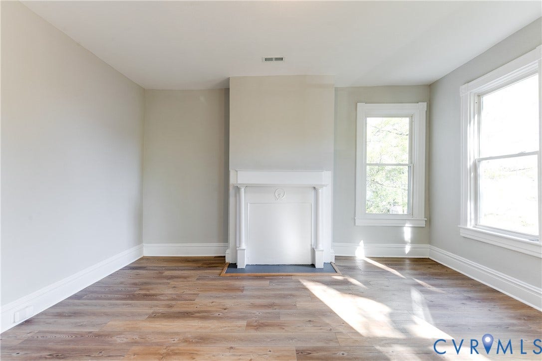 Light-toned walls with contrasting white trim, wood-finish flooring, a decorative fireplace, and multiple windows