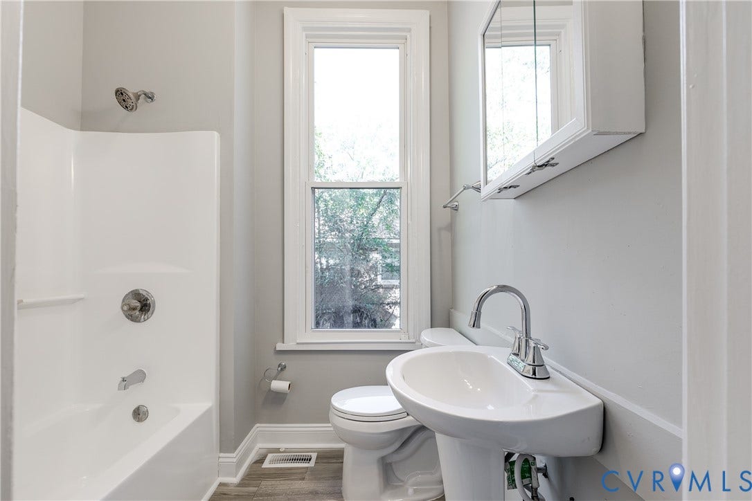 White pedestal sink, chrome fixtures, built-in medicine cabinet, white tub with shower, and wood-finish flooring