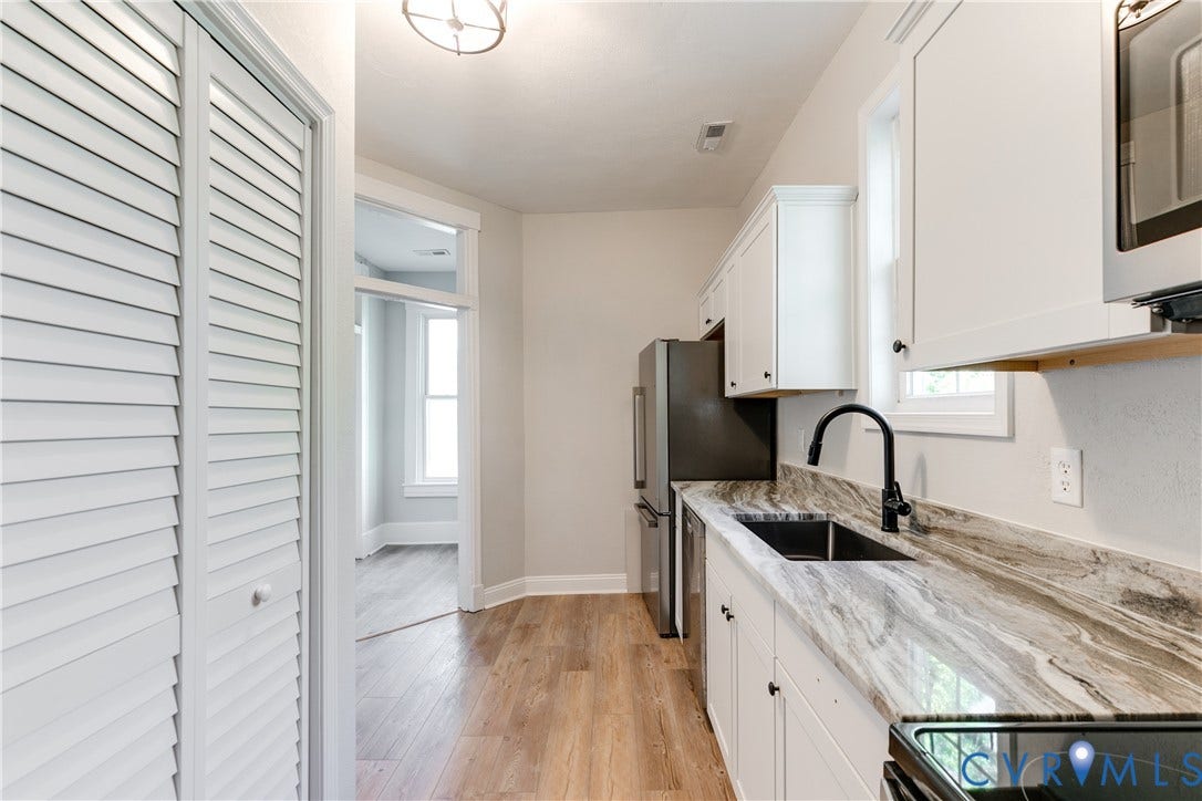 White cabinetry, wood-finish flooring, stainless steel refrigerator, dark faucet, and patterned countertop