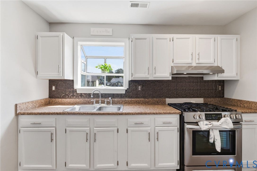 4429 Crown Squire Road, Henrico, VA 23231 White cabinetry with stainless steel hardware, a dual basin stainless steel sink, a stainless steel gas range, and a decorative backsplash