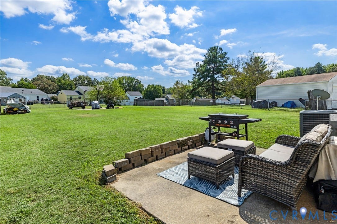 4429 Crown Squire Road, Henrico, VA 23231 Expansive grassy yard with a concrete patio, brick retaining wall, and a detached white storage building