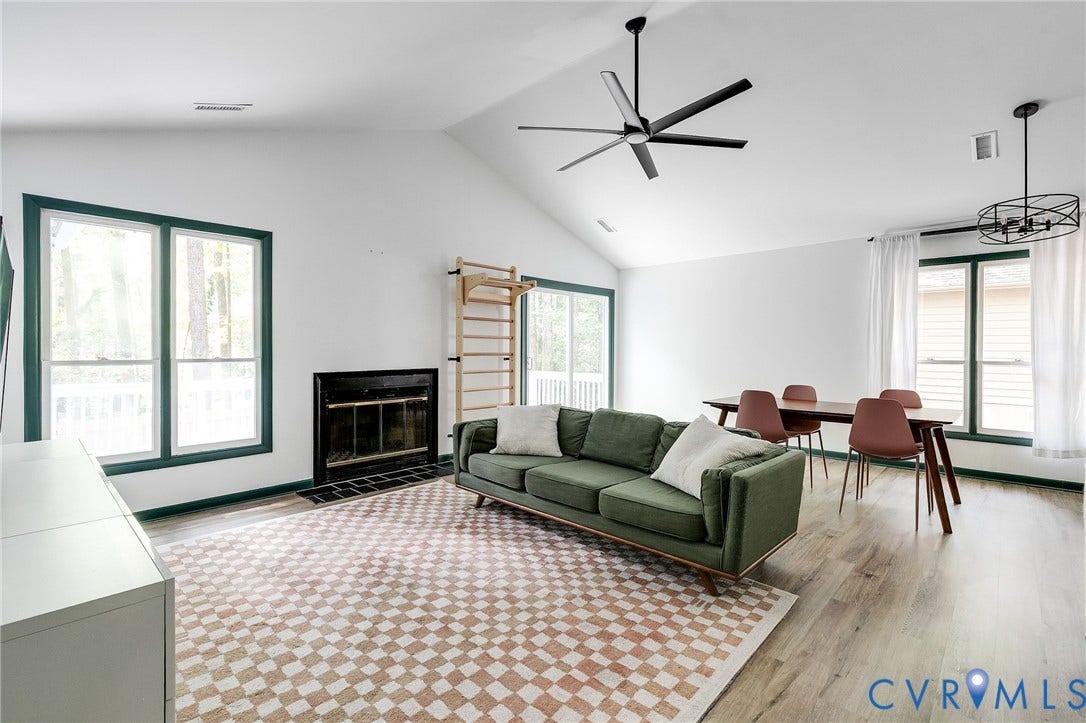 Vaulted ceiling, recessed fireplace, wood-finish flooring, multiple large windows, and a black ceiling fan