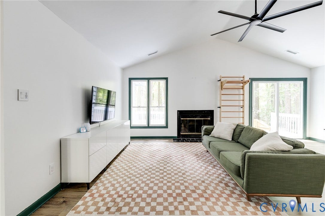 Vaulted ceiling with modern ceiling fan, wood-finish flooring, built-in fireplace, and sliding glass door
