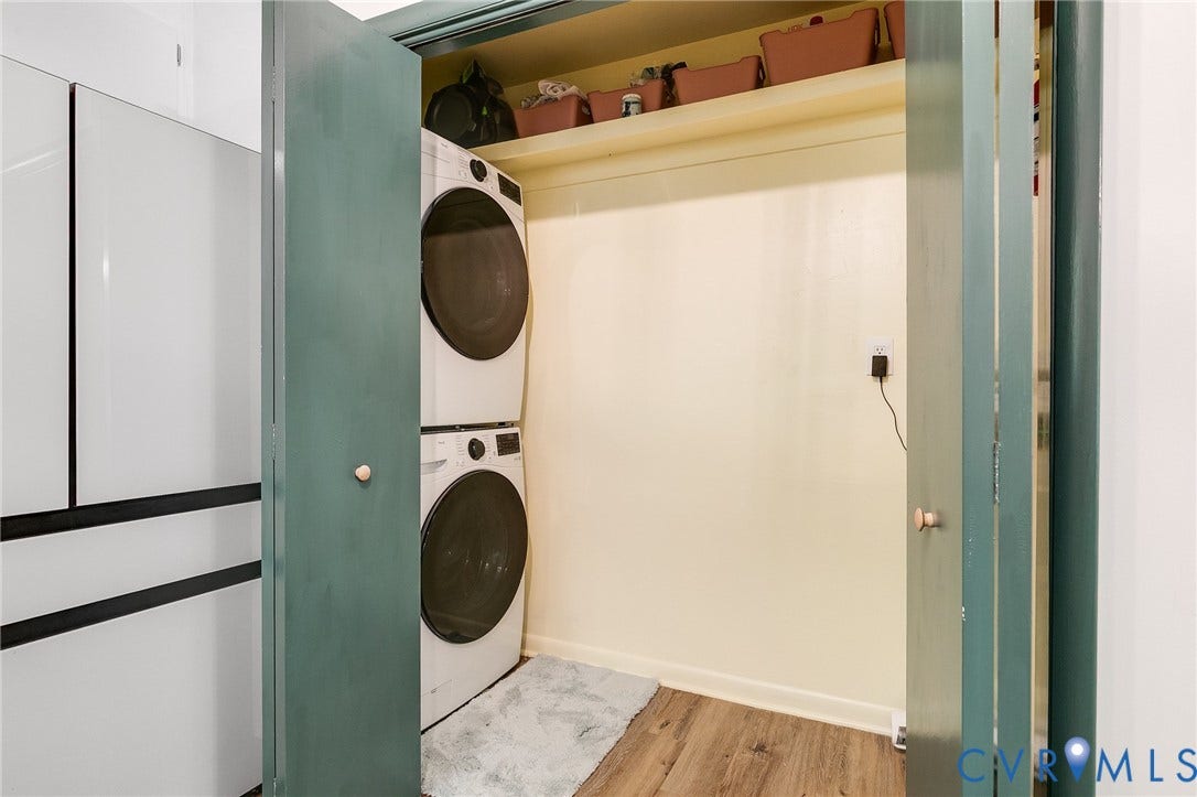 Dedicated laundry room featuring stacked front-load washers and dryers with white enamel finishes, wood shelving for storage, tile flooring, and soft ambient lighting for functional efficiency
