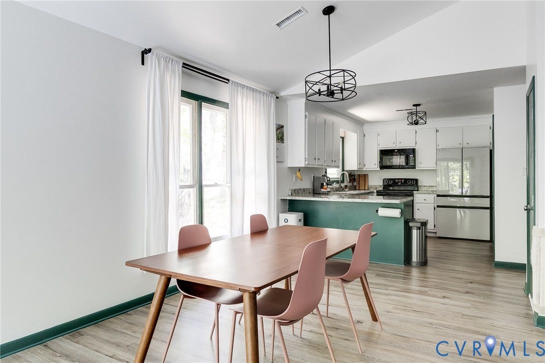 Open-concept kitchen and dining area featuring light wood-finish flooring, white cabinetry, a teal kitchen island, and black appliances