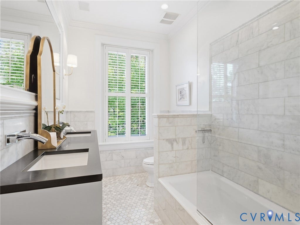 1829 Floyd Avenue, The Fan, Richmond, VA 23220 Double vanity with integrated sinks and dark countertops, white hexagon marble flooring, white subway tile bath surround, built-in bathtub, and plantation shutters