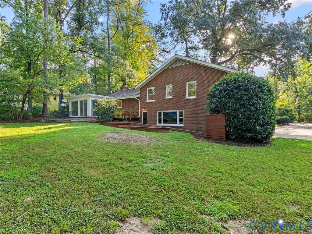 3436 Kenmore Road, Richmond, VA 23225 Brick exterior with white window frames and a sunroom addition featuring full-height windows, complemented by a wooden deck and mature landscaping