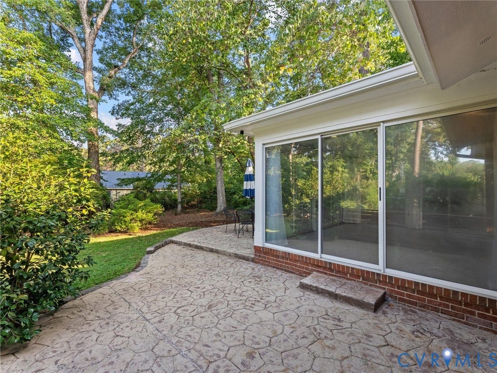 3436 Kenmore Road, Richmond, VA 23225 Expansive stamped concrete patio with direct access to a screened porch featuring large sliding glass doors, surrounded by mature trees and established landscaping