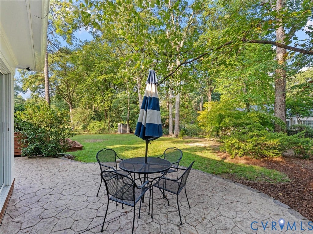 3436 Kenmore Road, Richmond, VA 23225 Patio with textured stone-finish surface, surrounded by mature trees, and an expansive lawn