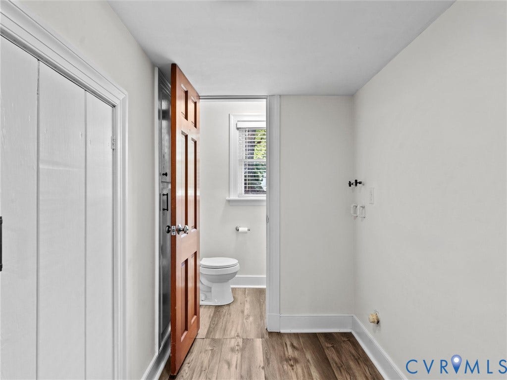 3436 Kenmore Road, Richmond, VA 23225 Wood-finish flooring with white baseboards, a wood-paneled door, and a partially visible toilet