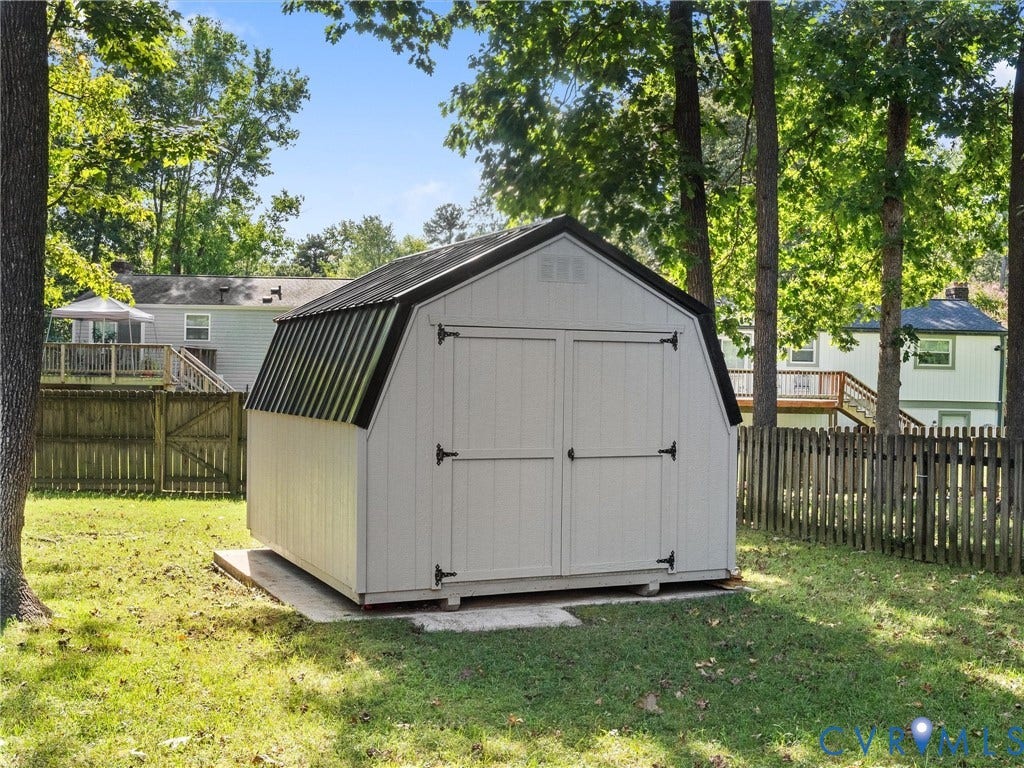 Gabled storage shed with a metal roof, double doors, and a wood privacy fence