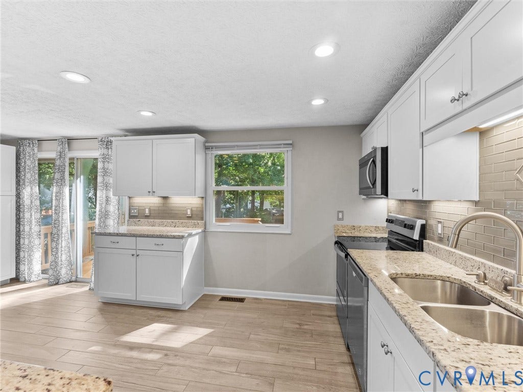 Kitchen featuring white cabinetry, light-toned countertops, a stainless steel sink, tile backsplash, and wood-finish flooring