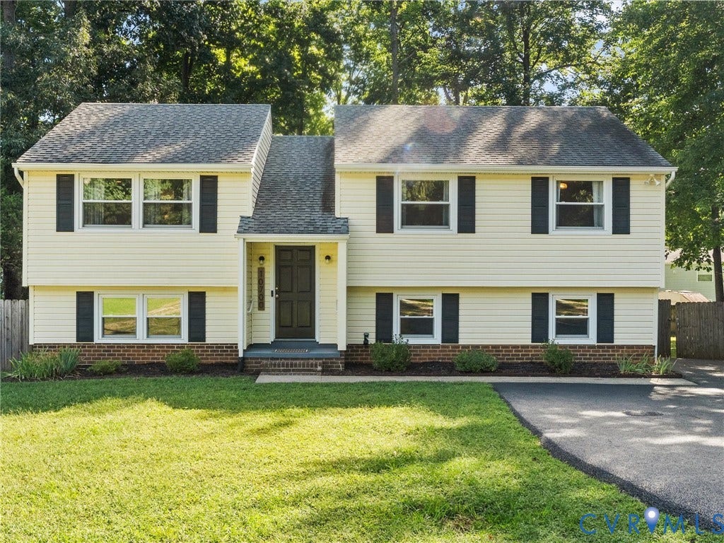 Two-story residence featuring light-colored siding, dark shutters, a front entry porch, and an attached driveway