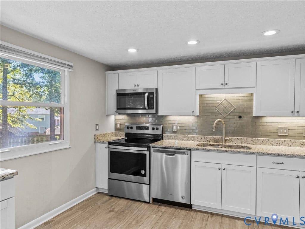 White shaker cabinetry, stainless steel appliances, speckled stone countertops, tile backsplash, and wood-finish flooring