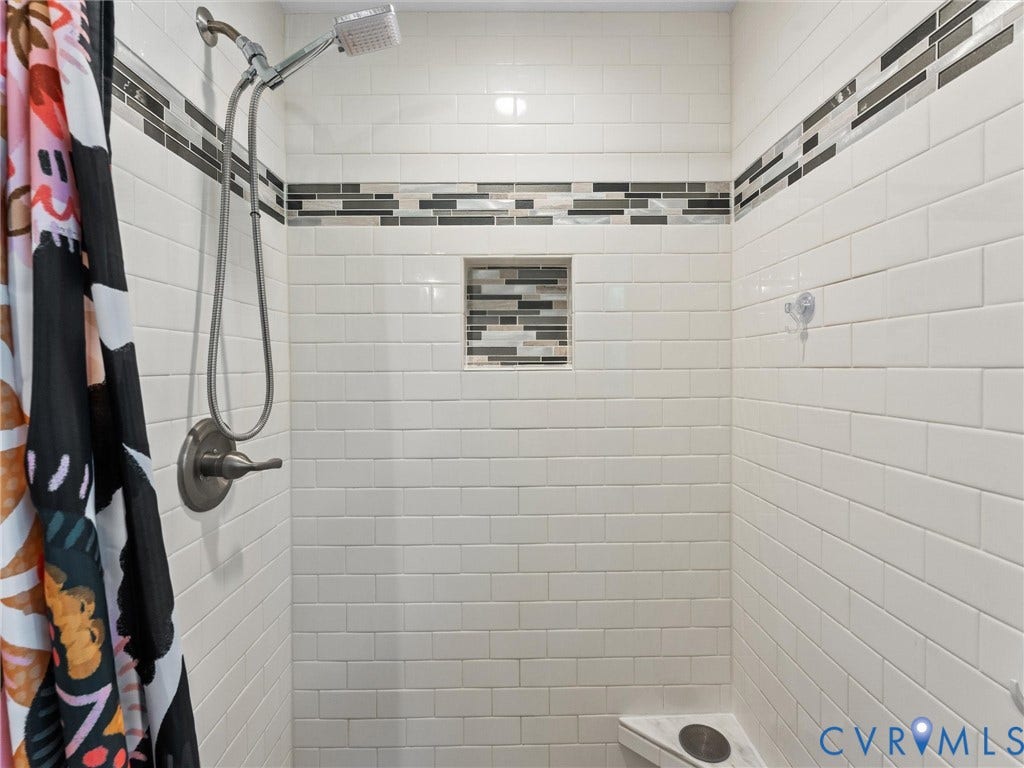 White subway tile shower enclosure featuring a decorative tile inlay and recessed niche