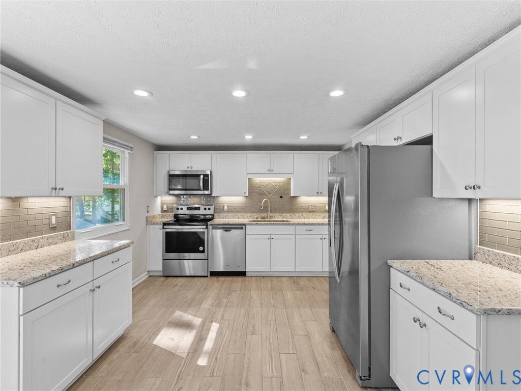 White cabinetry, light-toned wood-finish flooring, recessed lighting, and stainless steel appliances