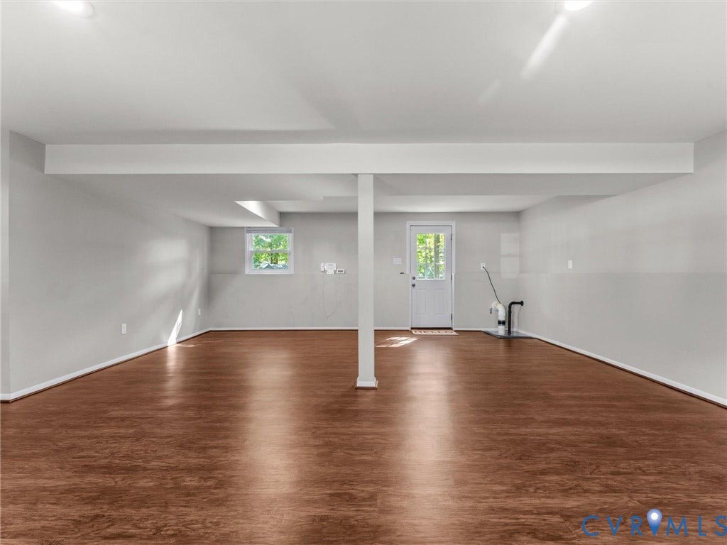 Expansive room featuring wood-finish flooring, white painted walls, recessed lighting, and a white paneled door with a glass insert