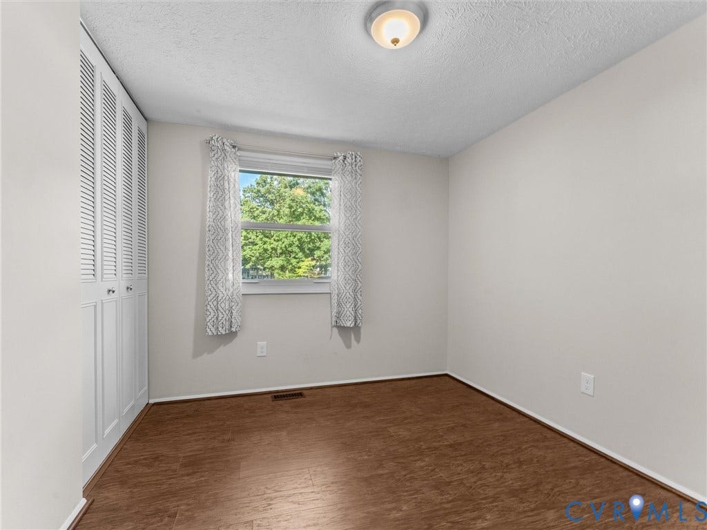 Wood-finish flooring, white walls, louvered closet doors, and flush-mount ceiling lighting