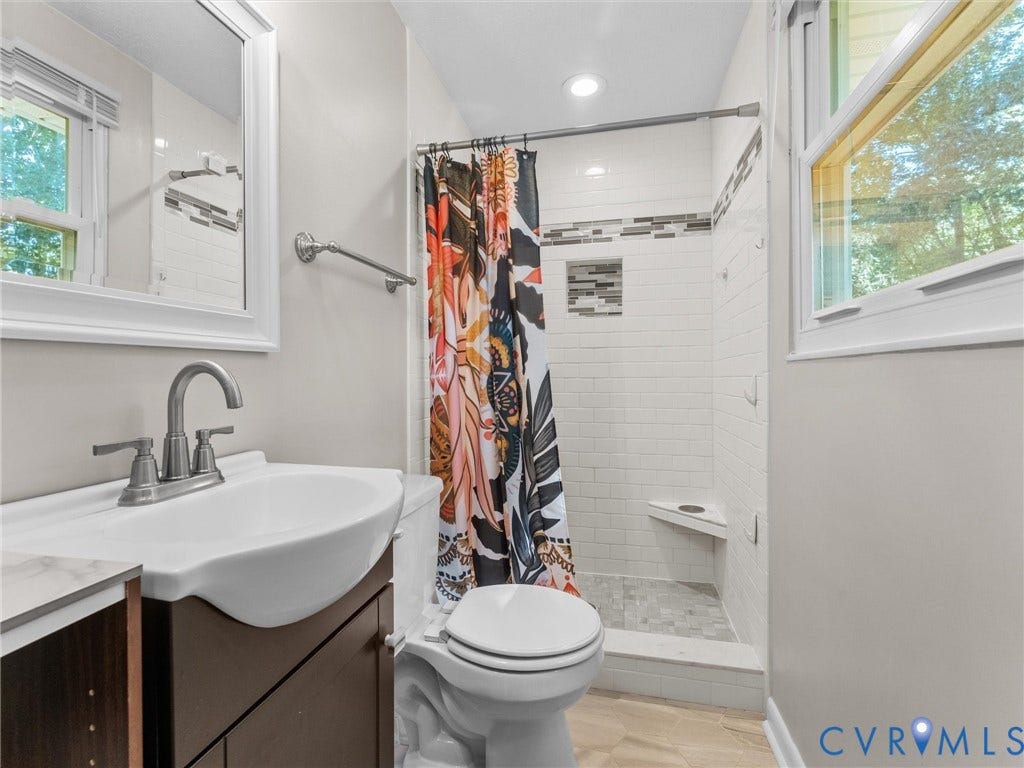 Bathroom featuring a white subway tile shower, built-in shower niche, shower bench, single vanity with a curved basin, and neutral floor tile