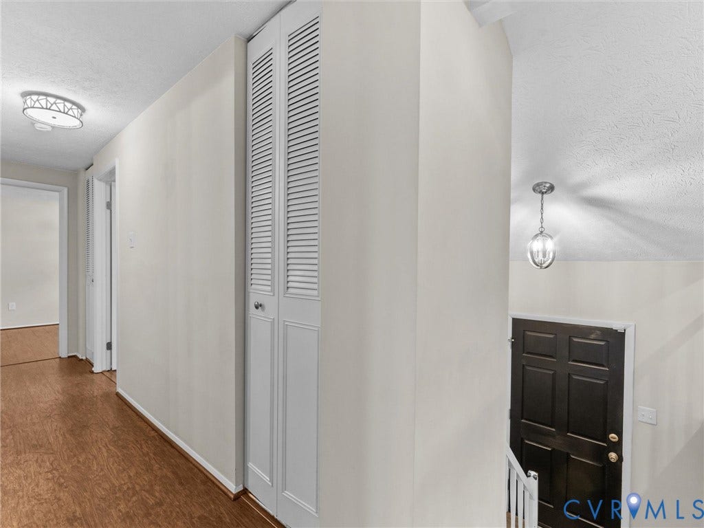 Hallway with wood-finish flooring, a flush-mount ceiling light, and louvered bi-fold doors