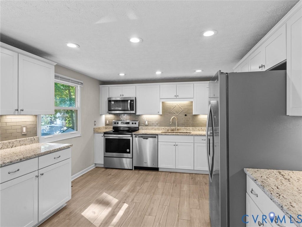 White cabinetry with stainless steel appliances, light-toned wood-finish flooring, recessed lighting, and granite countertops