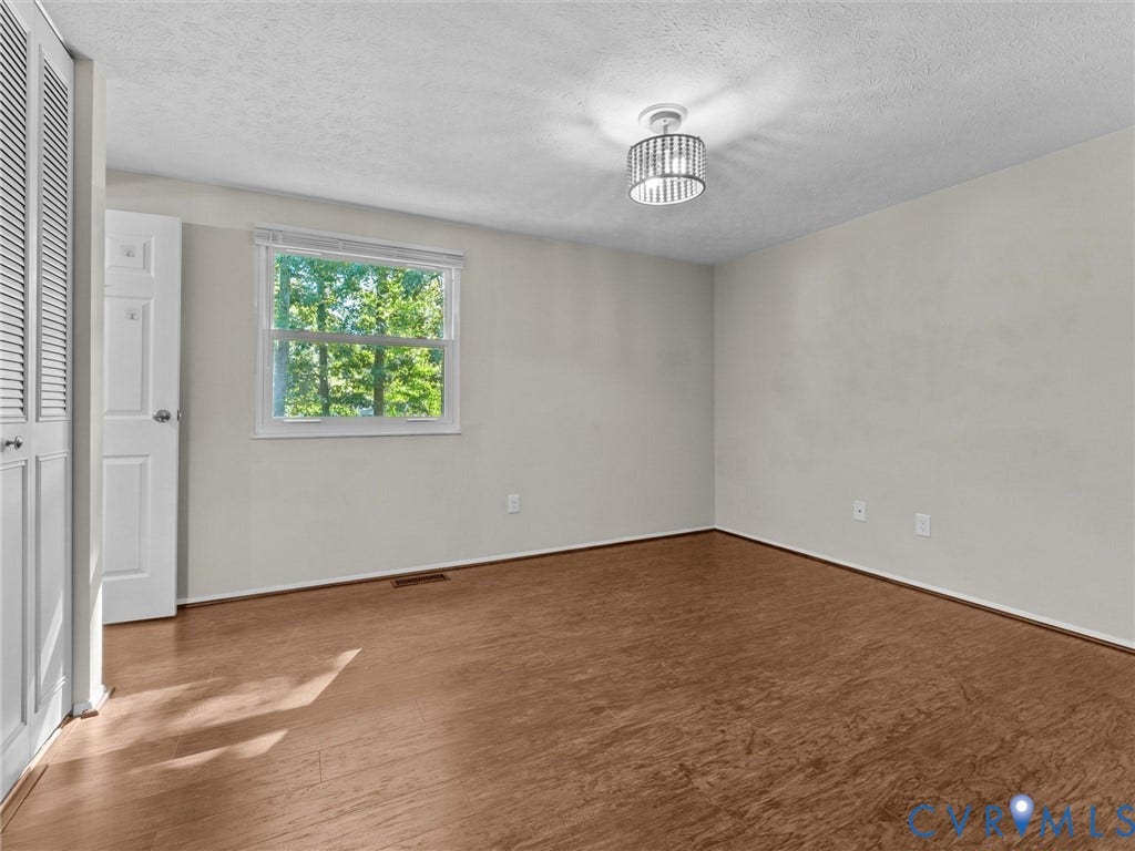 Wood-finish flooring with white baseboards, a window, a white door with a silver knob, and a decorative ceiling light