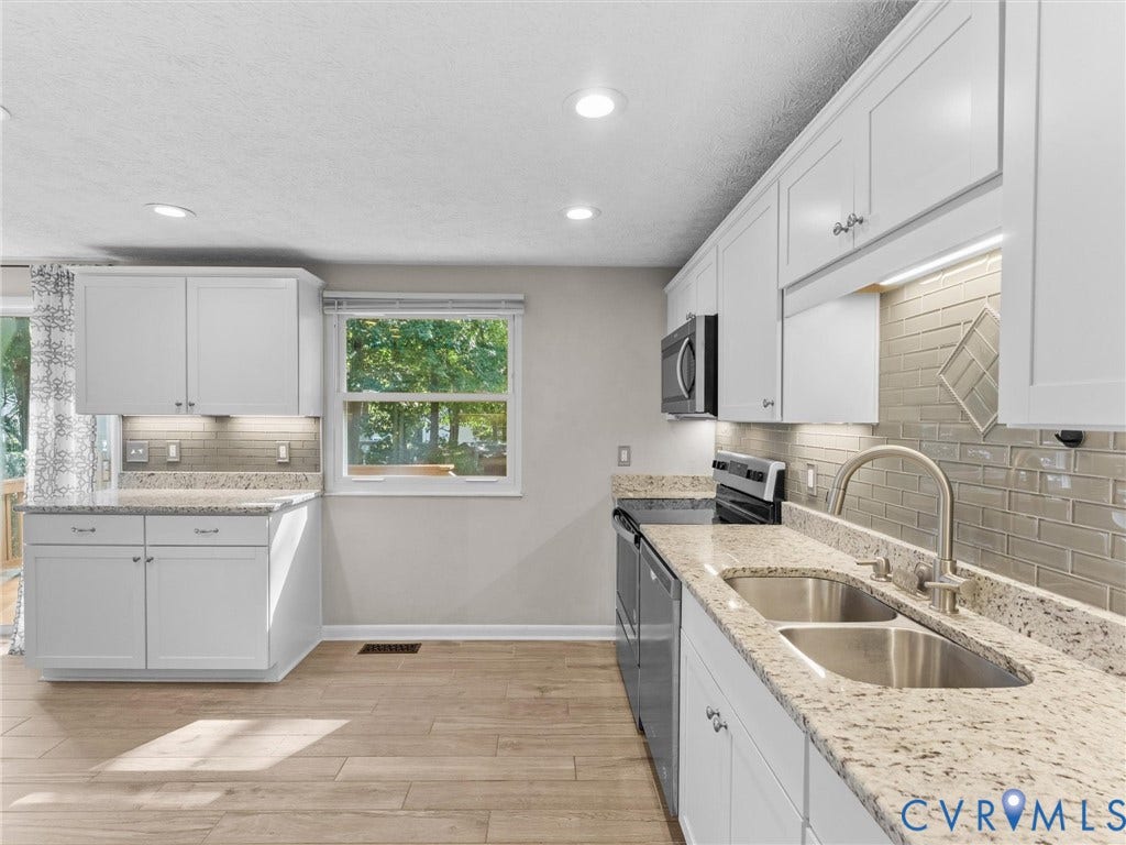 Contemporary kitchen featuring wood-finish flooring, white cabinetry, integrated stainless steel appliances, a double basin sink, and a tiled backsplash