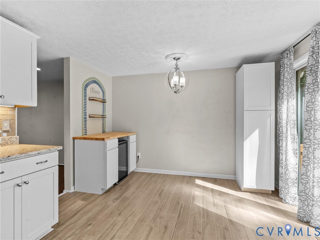 Wood-finish flooring throughout, white cabinetry with silver hardware, light-toned countertop, built-in shelving, and a modern ceiling fixture