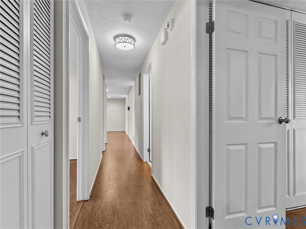 Hallway featuring wood-finish flooring, white walls, and a decorative flush-mount ceiling light