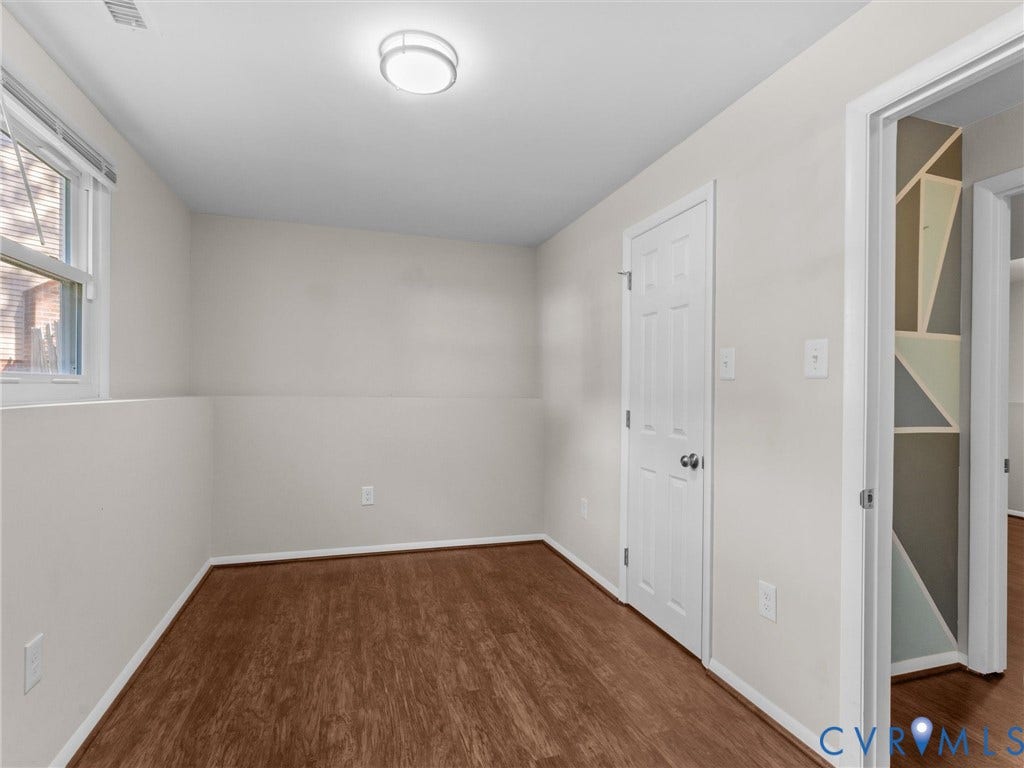 Wood-finish flooring, white paneled door, flush-mount ceiling light, and built-in shelving with geometric accents