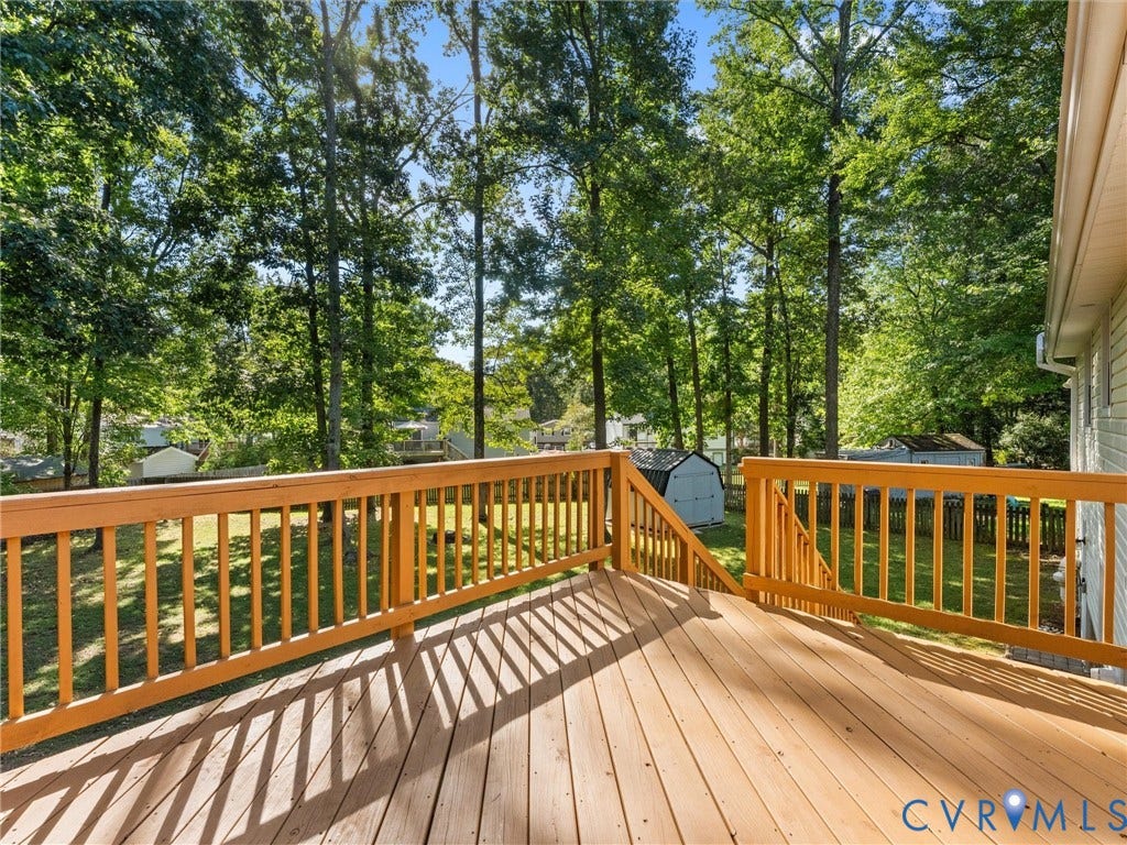 Wood-finish deck with a built-in railing and stairs, overlooking a grass lawn and mature trees