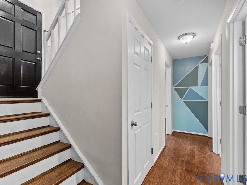 Wood-finish flooring, staircase with wood treads, white paneled doors, and a decorative accent wall