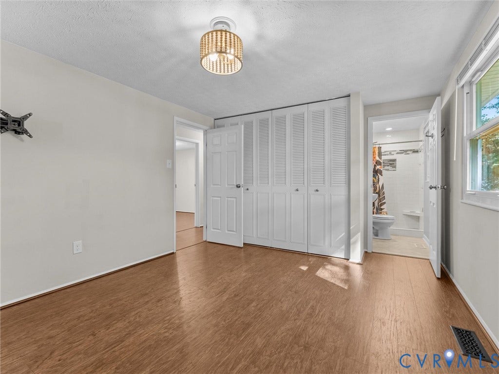 Wood-finish flooring throughout, white bi-fold closet doors, contemporary ceiling light fixture, and an attached full bathroom with a tiled shower