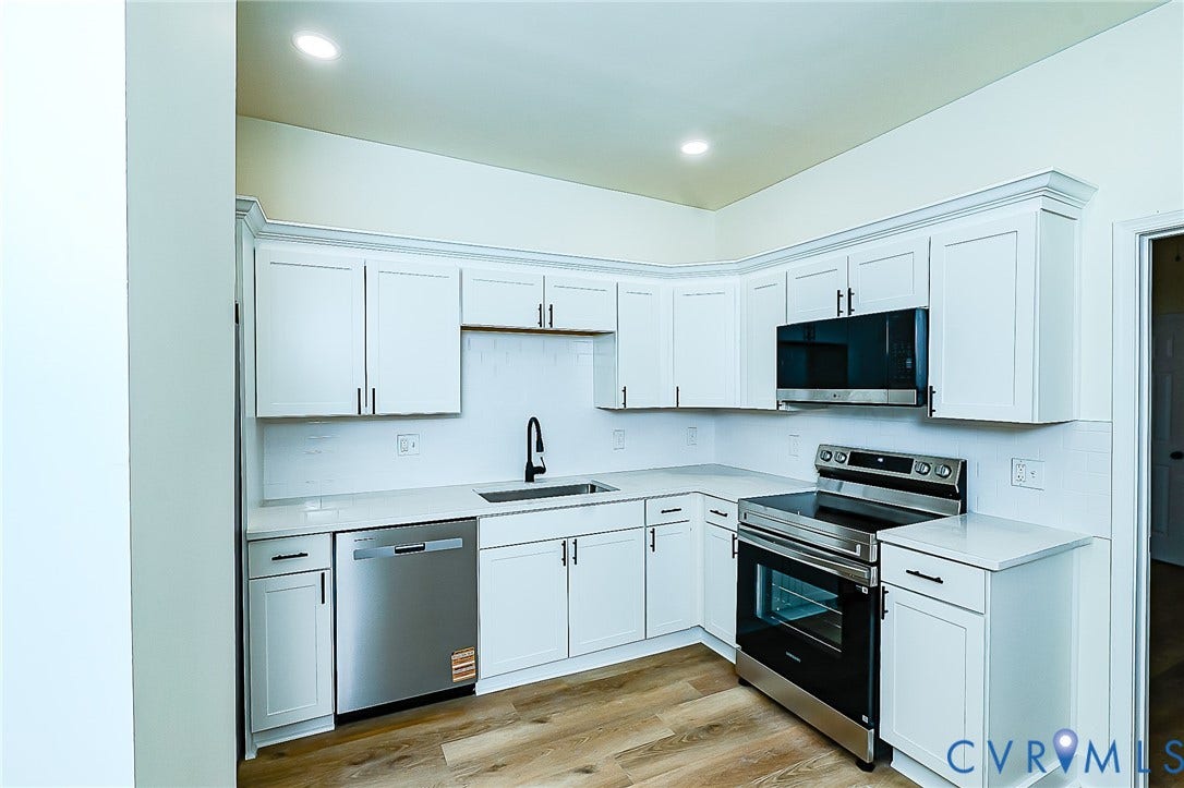 2813 Burfoot Street, Richmond, VA 23224 Modern kitchen featuring white shaker cabinetry, stainless steel appliances, a black pull-down faucet, and wood-finish flooring