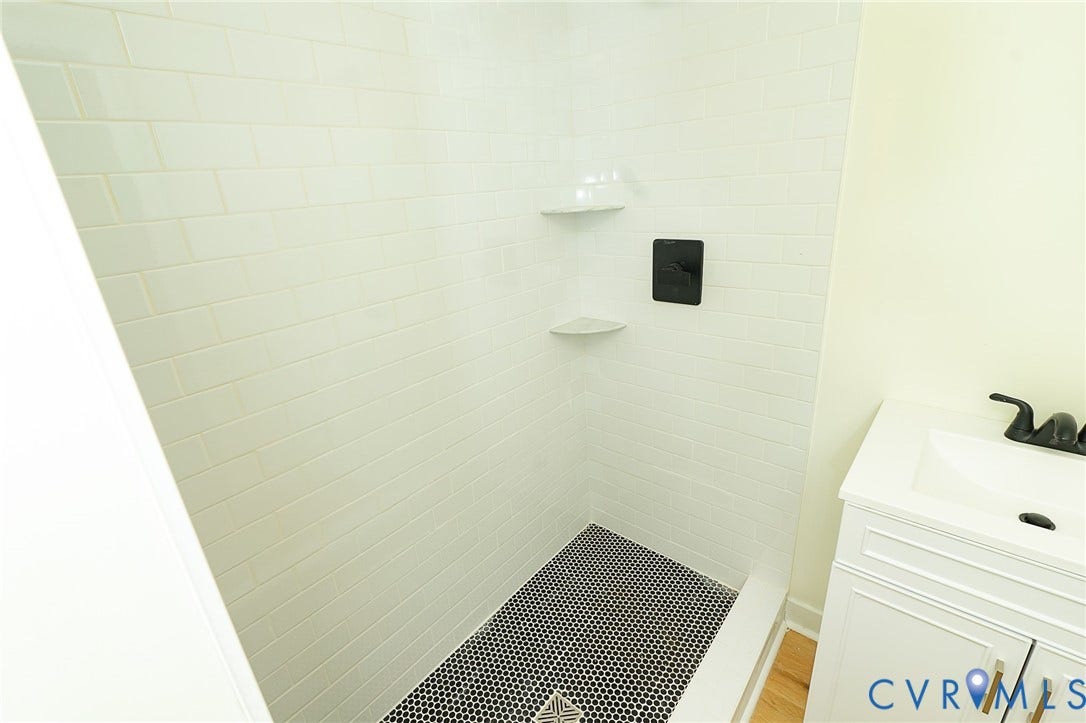 2813 Burfoot Street, Richmond, VA 23224 Shower stall featuring white subway tile, black penny tile flooring, and integrated corner shelves