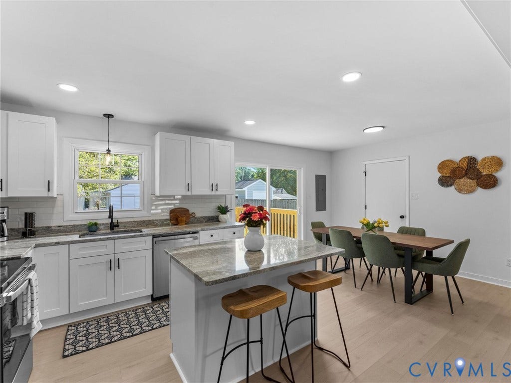 Open-concept kitchen featuring white cabinetry, light-toned wood-finish flooring, a central island with countertop, recessed lighting, and sliding glass door access to an outdoor area
