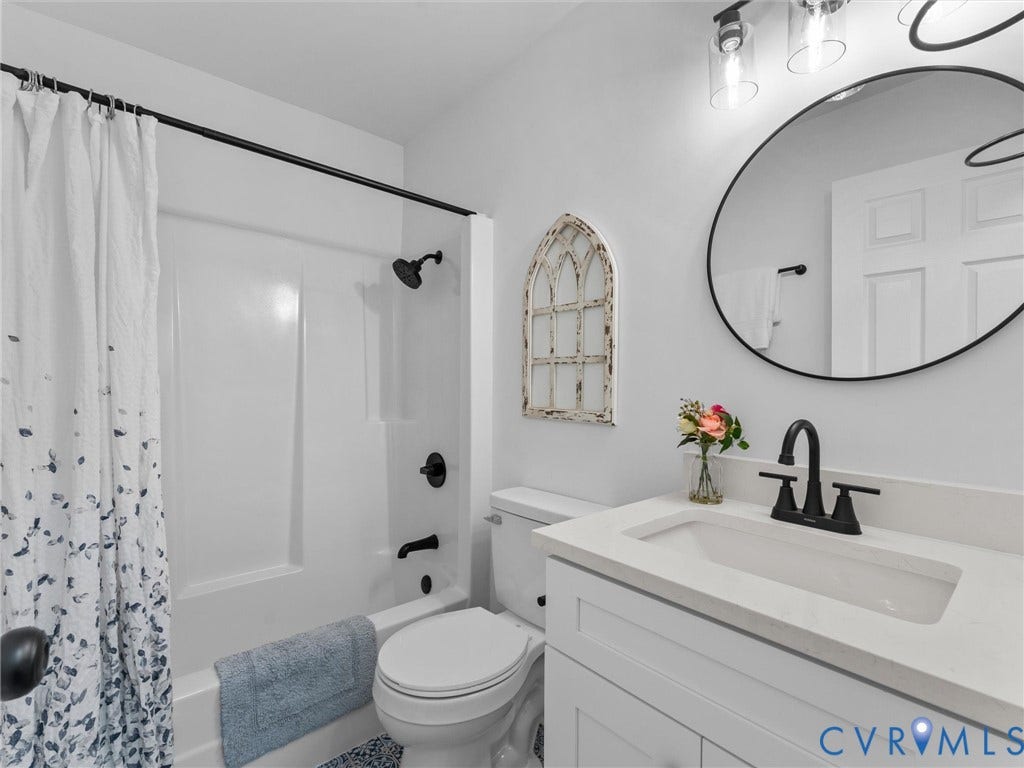 White vanity with an integrated sink, black faucet, circular mirror, and two-light fixture