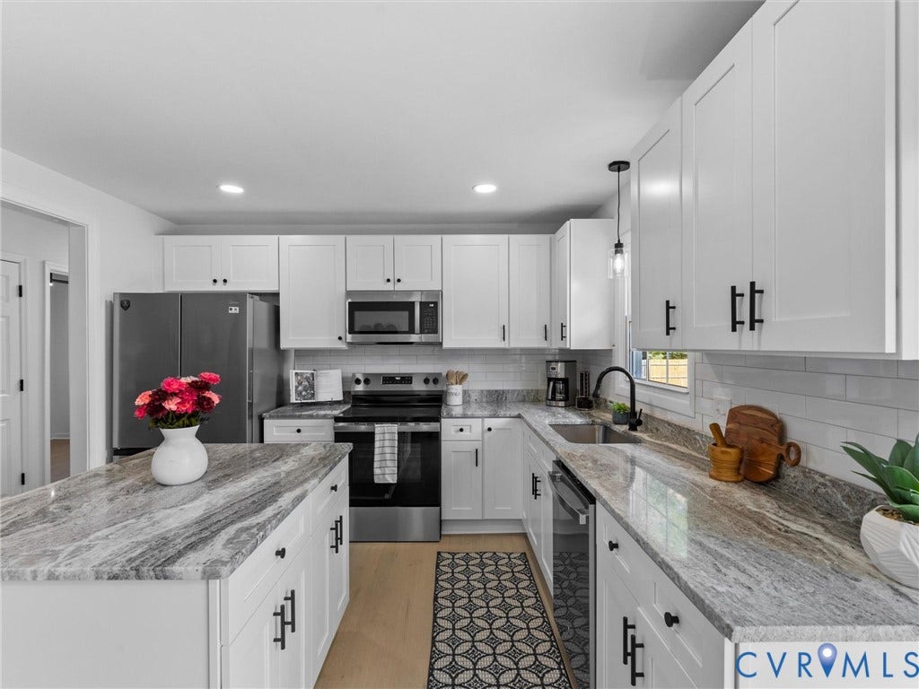 White cabinetry with dark hardware, stainless steel appliances, light wood-finish flooring, undermount sink with a black faucet, and patterned stone countertops
