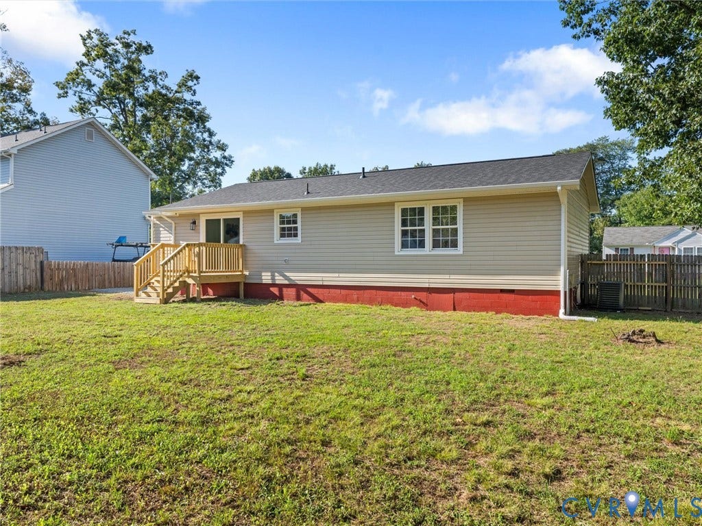 Expansive grassy yard with a wooden privacy fence, featuring a raised wooden deck with railings and steps