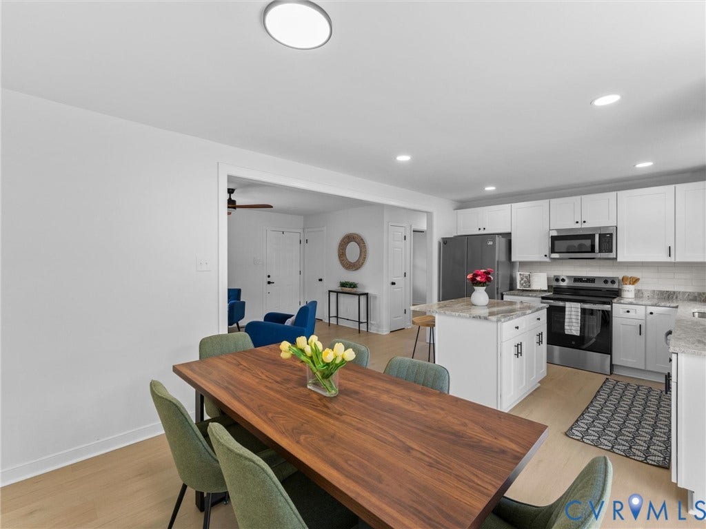 Spacious kitchen featuring white cabinetry, stone countertops, stainless steel appliances, and a central island