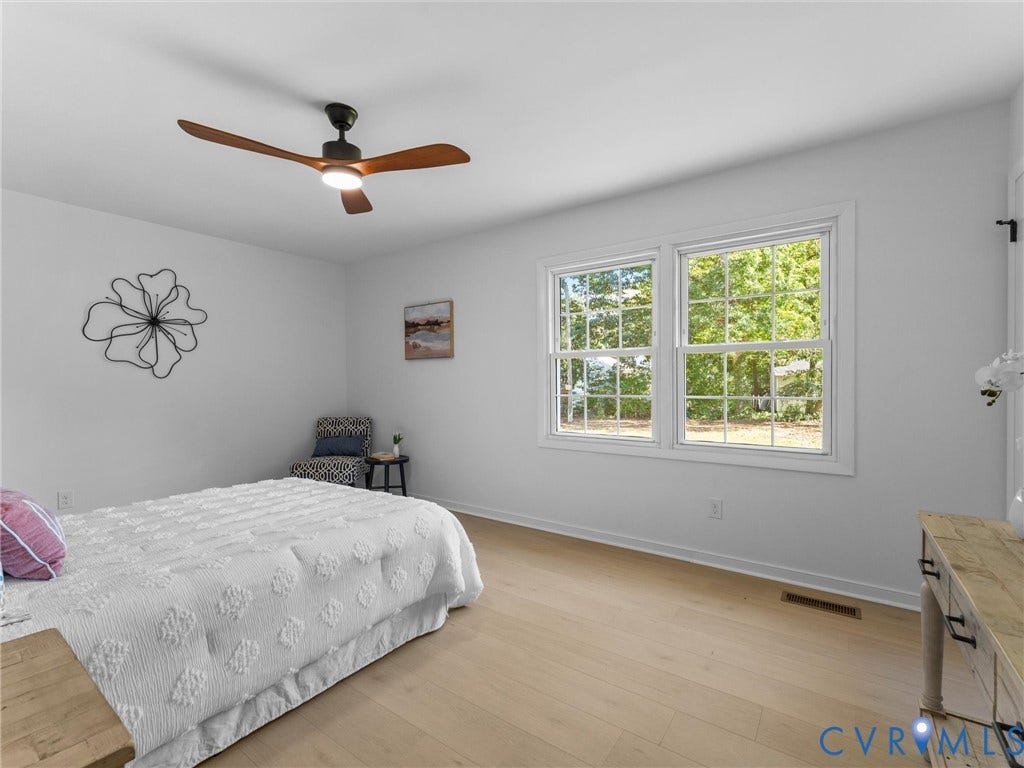 Wood-finish flooring, white walls, two large windows, and a ceiling fan with integrated lighting