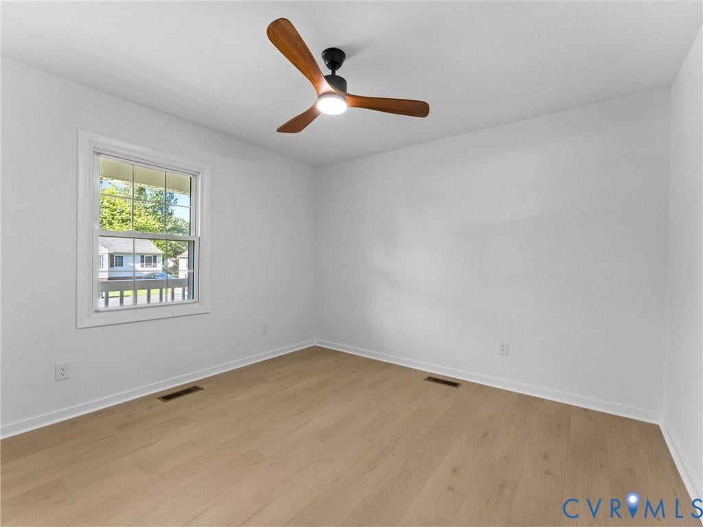 Light wood-finish flooring, white painted walls, and a modern ceiling fan with integrated lighting