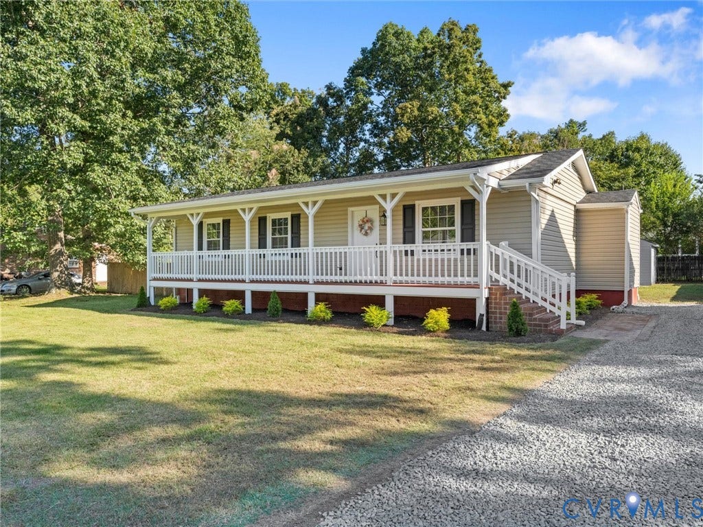 Ranch-style residence featuring light-colored siding, a covered front porch with white railings, a gravel driveway, and a front yard with manicured landscaping