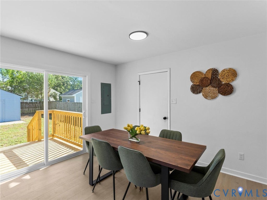 Sliding glass door leading to a wood deck, light-toned wood-finish flooring, and a flush-mount ceiling light